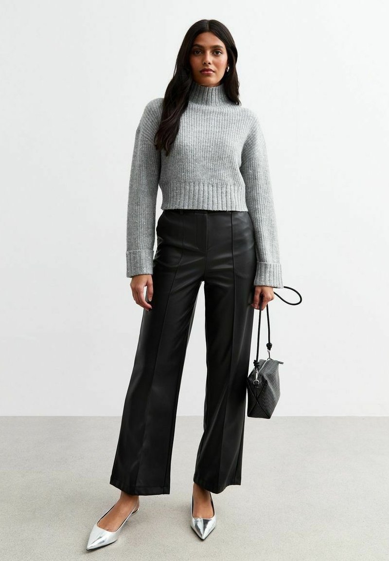 Maglione a collo alto grigio a coste, pantaloni a gamba larga in finta pelle nera a vita alta, décolleté argentati a punta, piccola borsa a tracolla in texture.