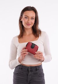 Red textured wallet with a black zipper and closure, featuring a small logo on the front. Compact, square shape, smooth finish with accents.