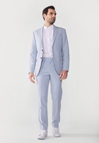 Helles blauer Nadelstreifenanzug mit maßgeschneidertem Schnitt, bestehend aus einem einreihigen Sakko, einer Hose mit flachem Vorderteil und einem weißen Hemd mit Knöpfen.