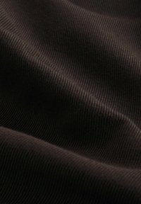 Tuvplāns tumši brūnas ribotas auduma, kurā redzamas mīkstas krokojuma un tekstūras ar smalkām slīpām līnijām.