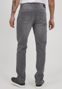 Jeans de mezclilla gris con corte recto, que cuentan con bolsillos traseros, sutiles desgastes y una textura suave. Combinados con zapatillas negras.