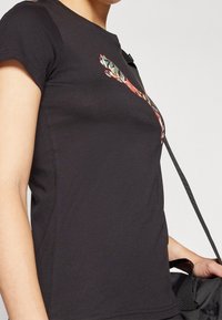 Camiseta negra de manga corta con un diseño gráfico colorido y estilizado en el lateral. Hecha de tela suave y elástica con un ajuste entallado.