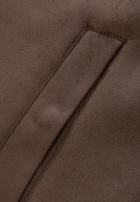 Bruin suède stof met een zachte textuur en een naaddetail dat verticaal loopt. Het oppervlak lijkt glad en mat.