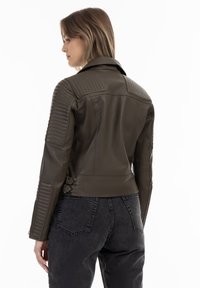 Brun læderjakke med ribbet skulderdetaljer og sidespænde, parret med mørke jeans, hvilket viser et tætsiddende design og glat tekstur.