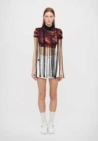 Top corto negro y naranja con detalles de flecos, combinado con una minifalda blanca. Zapatillas blancas y calcetines completan el atuendo.