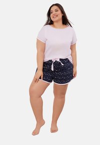 Jasnoróżowa bluzka z krótkim rękawem i okrągłym dekoltem, zestawiona z granatowymi szortami z białym wzorem gwiazdek i różowym paskiem w talii.