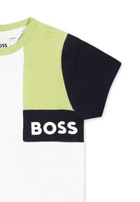 Korte mouwen T-shirt met groene, marineblauwe en witte panelen; heeft drukknoopsluitingen op de linker schouder en een wit "BOSS" logo.