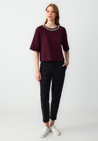 Bordeaux-kleurig shirt met korte mouwen en versierde halslijn, gecombineerd met zwarte tapse pantalons en witte sneakers. Glad stof, casual pasvorm.