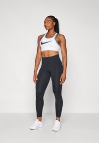 Sorte høy midje leggings kombinert med en hvit kort sports-bh med svarte detaljer og en sentral logo. Modell iført hvite joggesko.