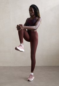 Sportinė apranga, susidedanti iš raštuotos tamsios palaidinės, bordo spalvos aukšto liemens leggingų ir rožinių sportbačių su baltais akcentais.