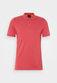Polo à manches courtes rouge corail avec deux boutons, col rabattu et logo discrètement embossé sur la poitrine.