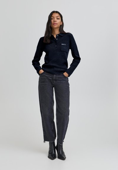 Jūras zils adīts polo ar apkakli, ar priekšējo kabatu un izšūtu tekstu. Saskaņots ar brīviem melniem džinsiem un kvadrātveida purngalu potīšu zābakiem.