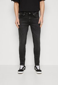 Svarta snäva jeans med bälteshällor, fem fickor och kontrasterande sömmar. Kombinerade med svarta och vita låga sneakers.