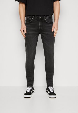 Jeans ajustados negros con pasadores para cinturón, cinco bolsillos y detalles de costura en contraste. Combinados con zapatillas bajas negras y blancas.
