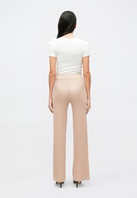 Bledoružové pletené nohavice so širokými nohavicami a vysokým pásom, v kombinácii s priliehavým bielym tričkom, pohľad zozadu.