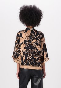Sort kimono-style skjorte med beige blomsterprint, korte ærmer og kontrasterende kant. Har "Karl" signaturdetalje på ryggen.