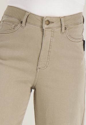 Beige broek met knopen aan de voorkant, taillebandlussen en zichtbare stiksels, gedragen met een wit topje in de broek gestopt.