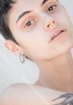 Orecchino a cerchio in argento con piccoli accenti di perle circolari. Il design è intricato, con una superficie testurizzata e una forma curva.