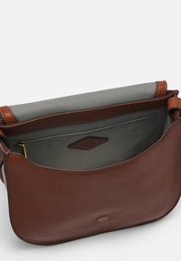 Brun læder crossover taske med klap åbnet, som viser gråt stofinteriør og en lynlåslomme med en læder mærketiket.