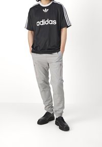 Musta urheilupaita, jossa on valkoinen "adidas"-logo ja raidat. Vaaleanharmaat lenkkihousut, joissa on vetoketjut sivuilla. Mustat nauhalliset kengät.