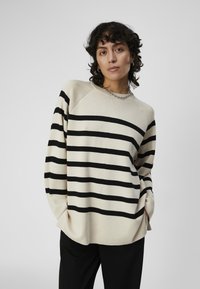 Maglione a maglia beige chiaro con strisce orizzontali nere, vestibilità casual, maniche raglan e scollatura rotonda. Texture liscia e design informale.