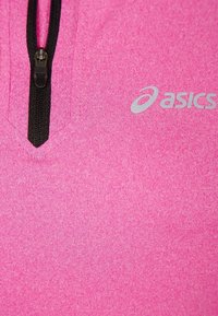 Fleecová mikina v jasně růžové barvě s černým zipem a šedým logem. Má měkkou texturu a výstřih ve tvaru V.