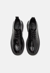Chaussures noires vernies à lacets avec semelles épaisses, vues de dessus sur un fond clair.
