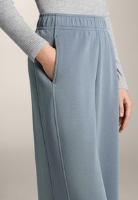 Svjetlomodré tepláky vyrobené z měkké tkaniny, s bočními kapsami a žebrovaným elastickým páskem pro pohodlné nošení.