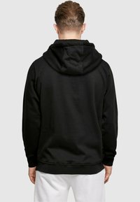 Svart hettegenser med snorhette, laget av mykt stoff. Har ribbestrikkede mansjetter og nederkant, med en jevn tekstur. Visning av baksiden.