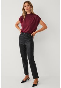 Top bordeaux a maniche corte abbinato a pantaloni neri in pelle sintetica a vita alta e tacchi neri a punta. Tessuto liscio e vestibilità strutturata.