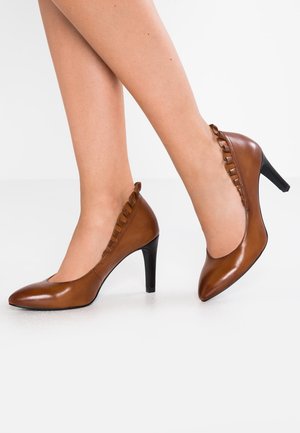 Brune læder højhælede sko med spids tå og dekorativ bølgekant langs åbningen. Hælen er cirka 7,5 cm høj.