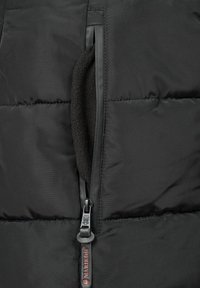 Black puffer jacket with a zippered pocket featuring a soft fleece lining, detailed with a black zipper pull and red branding near the zipper.