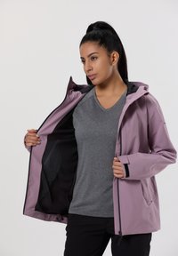 Giacca impermeabile di colore viola chiaro con cappuccio, caratterizzata da dettagli neri, fodera in rete e cerniera frontale, indossata sopra una maglietta grigia.