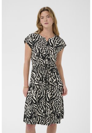 Woman wearing a black and white zebra print knee-length dress with short sleeves and a tied waist belt, standing against a plain background.