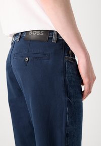 Μπλέ παντελόνι σε ναυτικό χρώμα με μίγμα από σταθερές και τζιν υφές. Διαθέτει δερμάτινη ετικέτα και μια μικρή πίσω τσέπη με κουμπί.