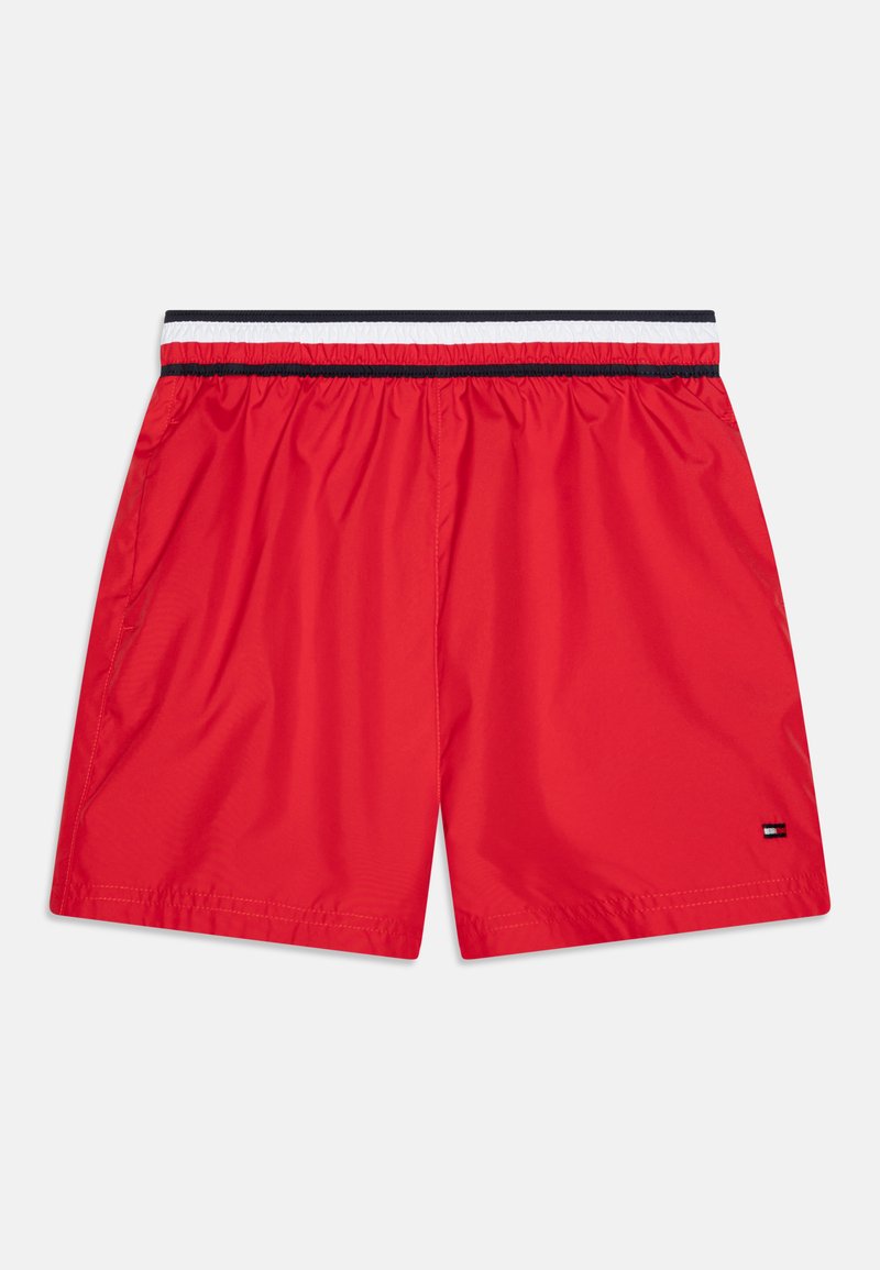 Red swim shorts made of lightweight fabric. Features an elastic waistband with black, white, and red stripes and a small logo tag on the hem.