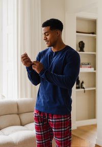 Camisa de manga larga azul marino con cuello redondo, combinada con pantalones de pijama a cuadros rojos. Ajuste casual, ligeramente metida en la cintura. Fondo de suelo de madera.