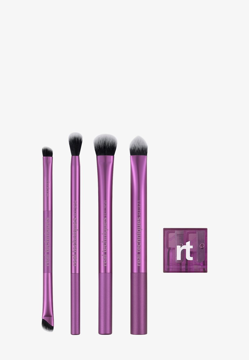 Quatre pinceaux de maquillage Real Techniques violets de différentes formes et tailles, accompagnés d'un taille-crayon "rt" violet sur fond blanc.