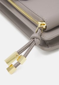 Szary syntetyczny worek na zamek błyskawiczny z złotymi akcentami, charakteryzujący się fakturowaną powierzchnią i węzłowym uchwytem zamka.
