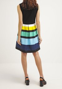 Sukienka bez rękawów z dopasowaną czarną górą i kolorową, paskowaną spódnicą w odcieniach żółtego, zielonego, czarnego, jasnoniebieskiego i ciemnoniebieskiego, z marszczonym detalem.
