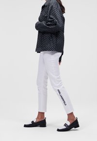 Black and white houndstooth patterned jacket, white slim-fit pants with "KARL LAGERFELD" printed, and black loafers with white accents.