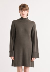 Πλεκτό φόρεμα σε σκούρο ελαιόλαδο πράσινο, με ψηλό λαιμό, υπερμεγέθη μανίκια με ριμπ μανσέτες, και χαλαρή γραμμή. Απαλή υφή με πλαϊνές σχισμές.