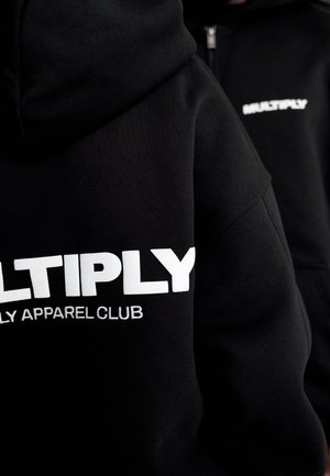 Hanorac negru cu inscripția „MULTIPLY” în litere albe îndrăznețe și „FAMILY APPAREL CLUB” în text mai mic, prezentând un material moale și texturat.
