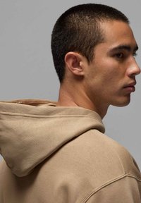 Felpa con cappuccio beige a maglia testurizzata, caratterizzata da un grande cappuccio e dettagli di cucitura visibili, mostrata da un'angolazione laterale.