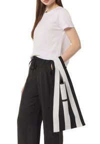 Helles rosa, enganliegendes T-Shirt, kombiniert mit schwarzen Hose mit elastischem Bund. Eine schwarz-weiß gestreifte Tasche hängt an der Hand und hat ein schickes Design.