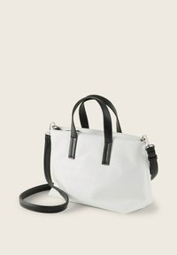 Sac à main blanc avec des accents noirs, fabriqué en matériau lisse. Comprend deux poignées courtes, une bandoulière réglable et un logo en relief.
