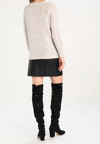 Suéter de punto gris claro con mangas largas, acabado texturizado, combinado con una minifalda de cuero sintético negra y botas negras por encima de la rodilla.