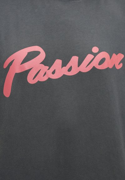 Γκρι βαμβακερό t-shirt με μεγάλο, καλλιγραφικό ροζ κείμενο που γράφει «Passion» στο στήθος. Λείο υλικό με στρογγυλή λαιμόκοψη.