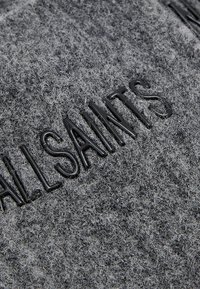 Grijze viltstof met verhoogde zwarte letters die "ALLSAINTS" spellen. De textuur lijkt zacht en enigszins fuzzy.
