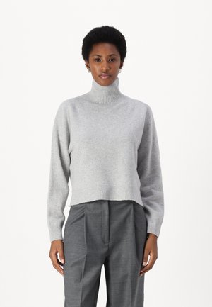 Grå, kort turtleneck genser med ribbestrikkede mansjetter og kant, laget av et mykt materiale. Brukt sammen med grå skræddersydde bukser.